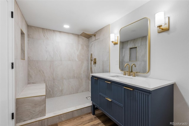 bathroom with wood-type flooring, tiled shower, and vanity