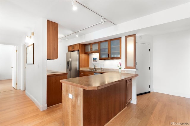 kitchen with track lighting, light wood-type flooring, brown cabinets, stainless steel fridge with ice dispenser, and a sink