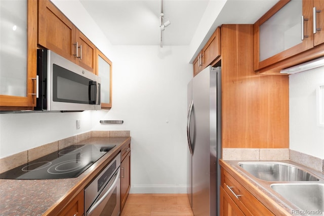 kitchen featuring brown cabinetry, track lighting, baseboards, light wood-style floors, and appliances with stainless steel finishes