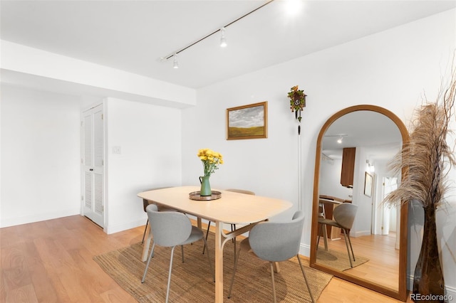 dining space with arched walkways, baseboards, track lighting, and light wood finished floors