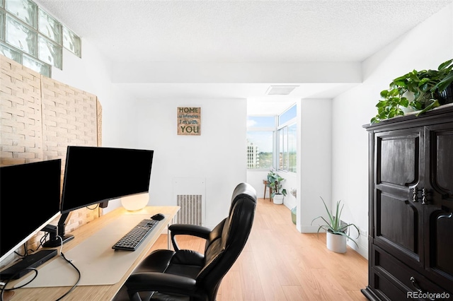 office area with visible vents, a textured ceiling, light wood finished floors, and baseboards