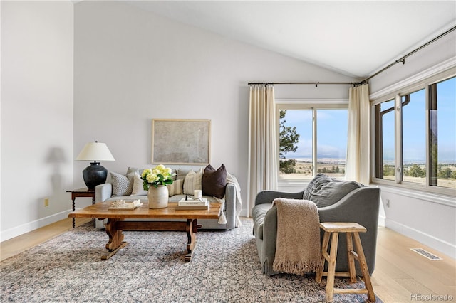 living area featuring visible vents, light wood-style floors, plenty of natural light, and vaulted ceiling