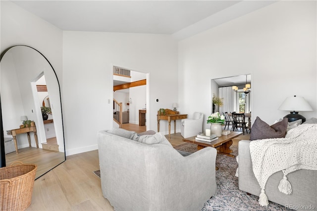 living area with an inviting chandelier, high vaulted ceiling, light wood-style flooring, visible vents, and stairway