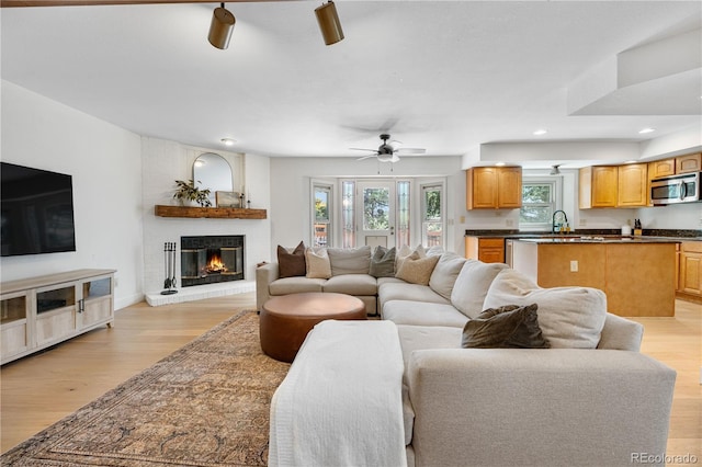 living area with a brick fireplace, a ceiling fan, recessed lighting, and light wood finished floors