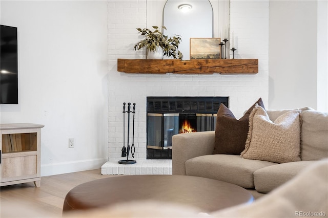 living room featuring a brick fireplace, baseboards, and wood finished floors