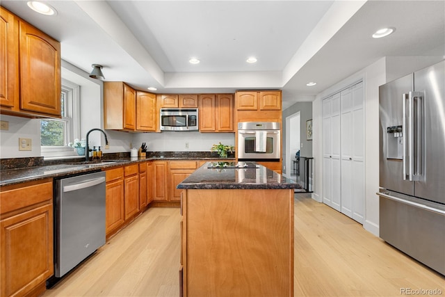 kitchen with a kitchen island, dark stone counters, a sink, light wood finished floors, and appliances with stainless steel finishes