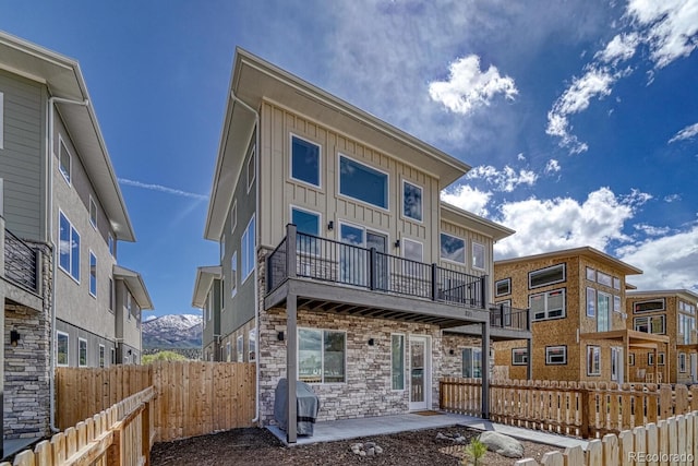 rear view of property featuring board and batten siding, fence private yard, stone siding, and a balcony