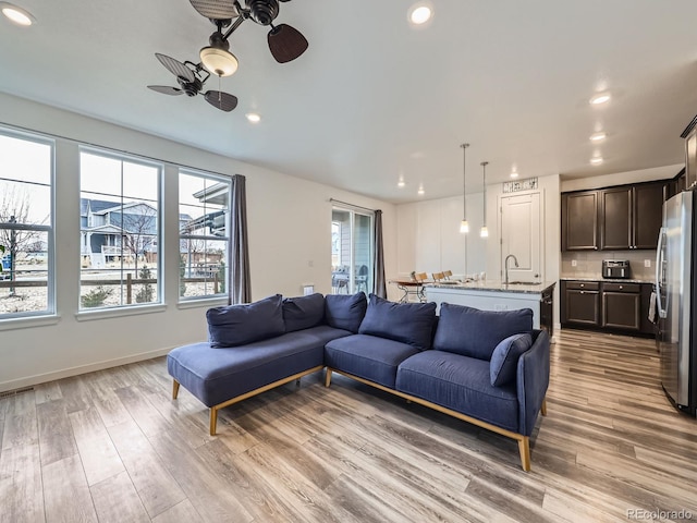 living room featuring sink, ceiling fan, light wood-type flooring, and plenty of natural light