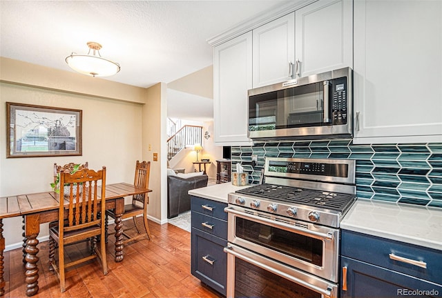 kitchen featuring white cabinetry, blue cabinetry, stainless steel appliances, and light hardwood / wood-style flooring