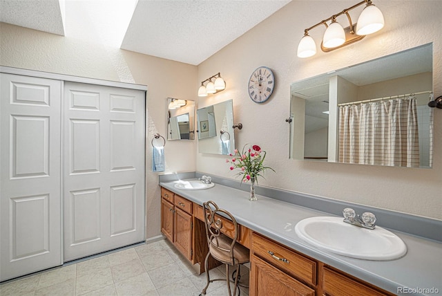 full bath with a textured ceiling, double vanity, a sink, and a textured wall