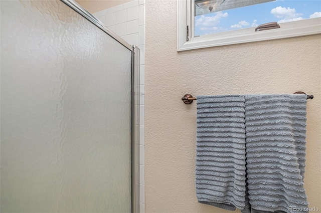 room details featuring a shower with door and a textured wall