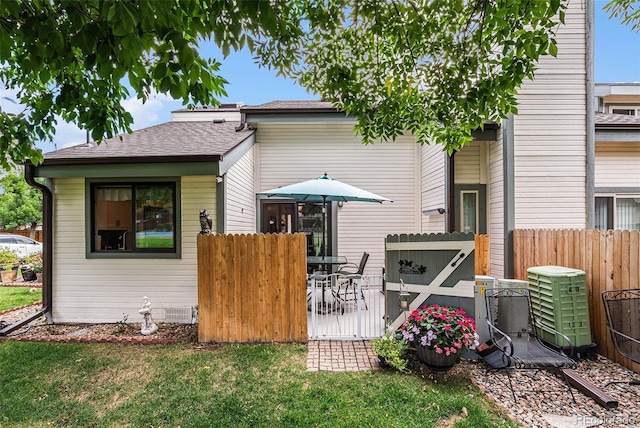 back of property with a shingled roof, a wooden deck, central AC unit, fence, and a yard