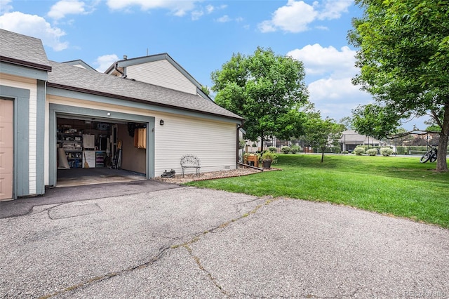 view of side of home with a yard, roof with shingles, driveway, and a garage