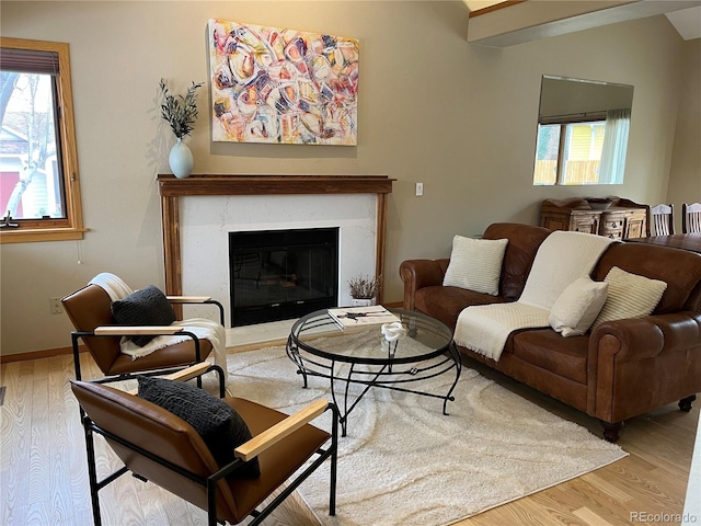 living room featuring a high end fireplace, vaulted ceiling, baseboards, and wood finished floors