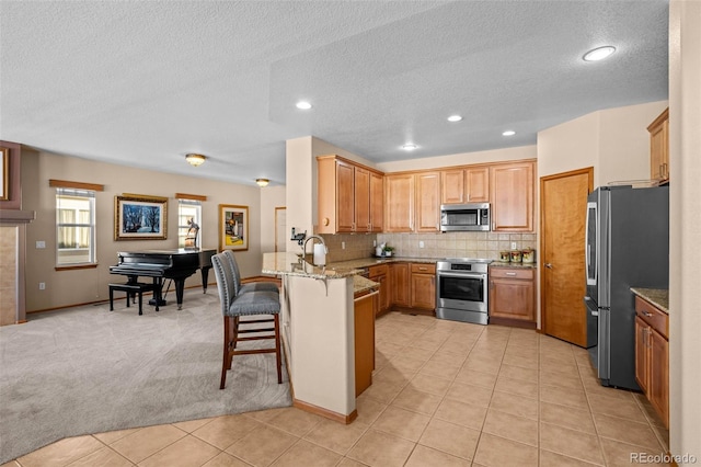 kitchen with a kitchen bar, kitchen peninsula, appliances with stainless steel finishes, backsplash, and light stone counters