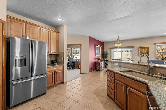 kitchen with stainless steel fridge with ice dispenser, light tile patterned floors, light stone counters, and sink