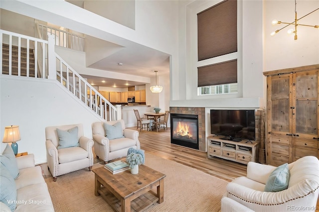 living room with light hardwood / wood-style floors, a towering ceiling, and an inviting chandelier