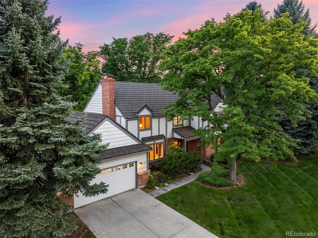 view of front facade featuring a garage, driveway, a lawn, stucco siding, and a chimney