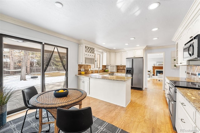 kitchen with light stone counters, white cabinets, ornamental molding, appliances with stainless steel finishes, and light wood finished floors