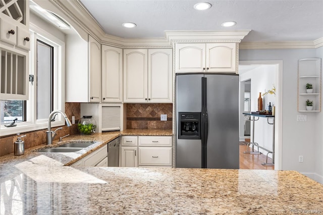 kitchen featuring a sink, ornamental molding, appliances with stainless steel finishes, backsplash, and light stone countertops