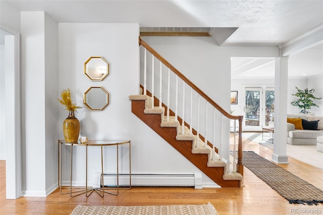 stairs featuring ornate columns, baseboards, a baseboard heating unit, and wood finished floors