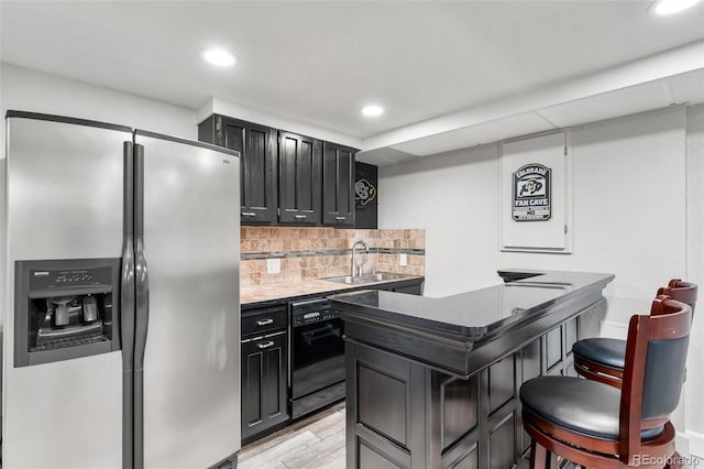 kitchen featuring black dishwasher, tasteful backsplash, dark cabinetry, stainless steel refrigerator with ice dispenser, and a sink