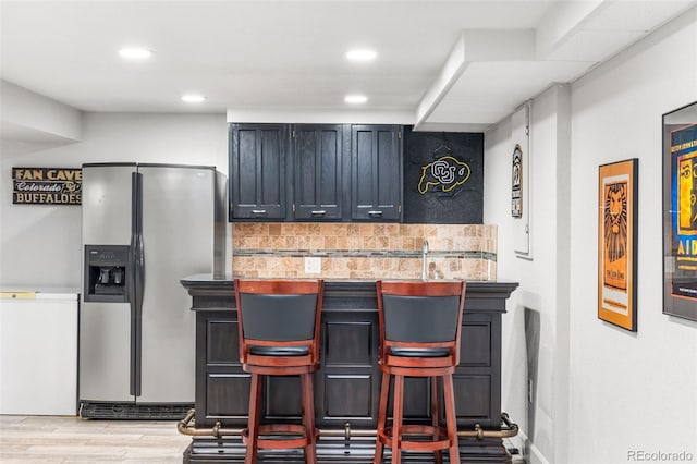 kitchen featuring light wood finished floors, stainless steel fridge, decorative backsplash, a kitchen bar, and recessed lighting