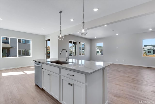 kitchen with light hardwood / wood-style floors, light stone counters, white cabinets, sink, and a kitchen island with sink