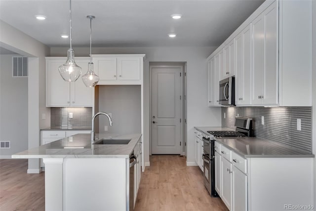 kitchen with sink, an island with sink, white cabinetry, appliances with stainless steel finishes, and decorative light fixtures