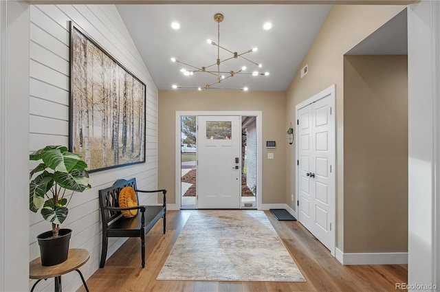 foyer entrance featuring a notable chandelier, lofted ceiling, wooden walls, and light wood-type flooring