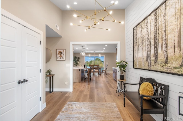 hall featuring a high ceiling, sink, a notable chandelier, and light hardwood / wood-style flooring