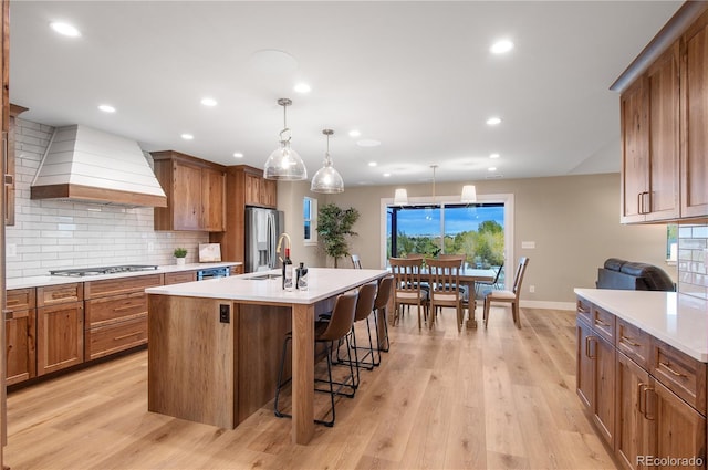 kitchen featuring pendant lighting, a breakfast bar, appliances with stainless steel finishes, premium range hood, and a center island with sink