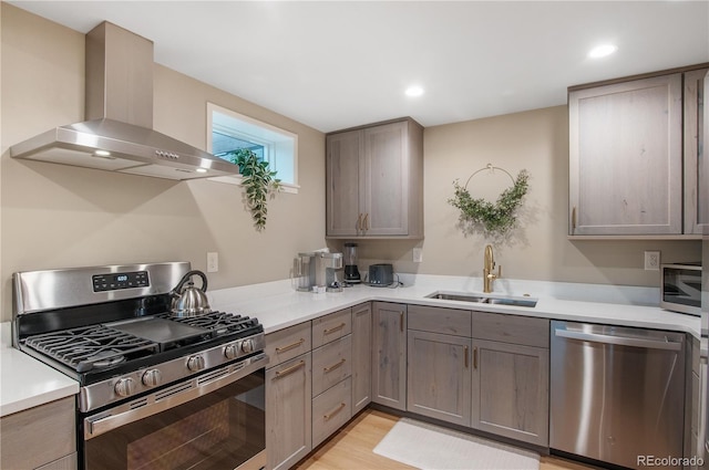 kitchen featuring sink, light hardwood / wood-style flooring, gray cabinetry, stainless steel appliances, and wall chimney exhaust hood