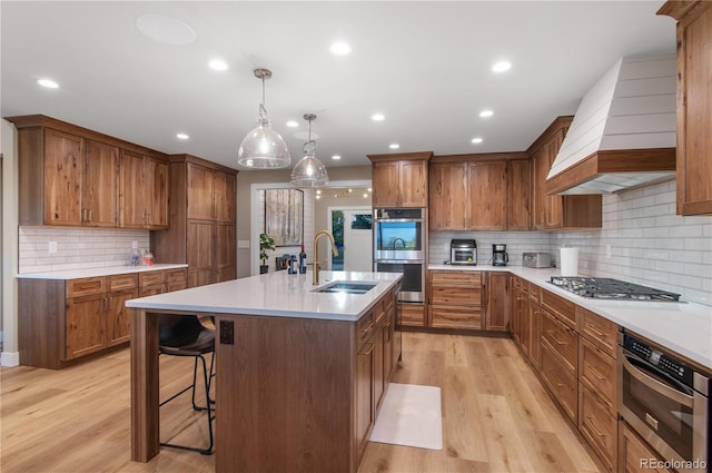 kitchen featuring sink, appliances with stainless steel finishes, hanging light fixtures, a center island with sink, and custom exhaust hood