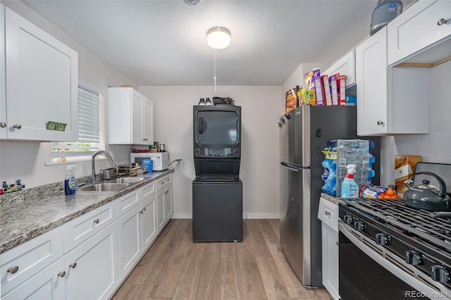 kitchen with light wood-type flooring, stacked washer / dryer, white cabinets, gas stove, and sink