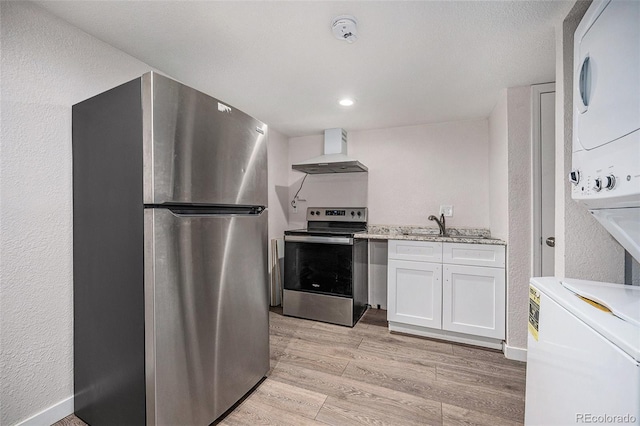 kitchen with stacked washer and dryer, appliances with stainless steel finishes, wall chimney exhaust hood, light hardwood / wood-style floors, and white cabinets