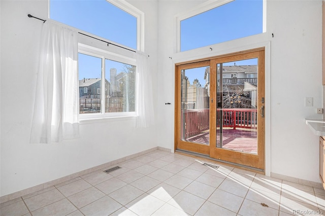 doorway to outside with visible vents, a towering ceiling, baseboards, and light tile patterned flooring