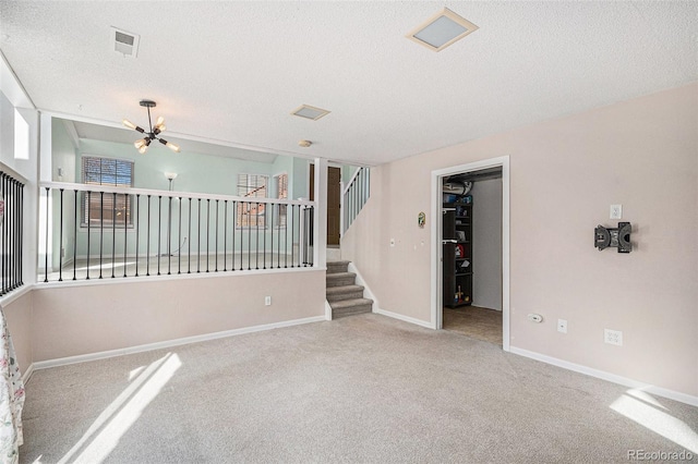 carpeted empty room featuring a textured ceiling, a chandelier, visible vents, baseboards, and stairs