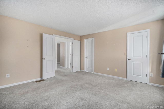 spare room featuring carpet floors, visible vents, baseboards, and a textured ceiling