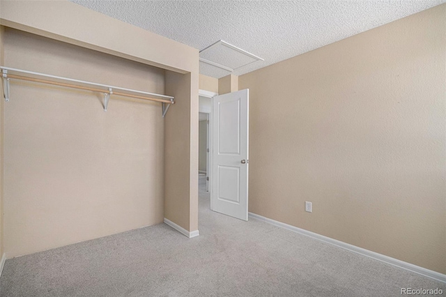 unfurnished bedroom featuring a closet, attic access, carpet flooring, a textured ceiling, and baseboards