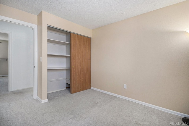 unfurnished bedroom with a closet, light colored carpet, a textured ceiling, and baseboards