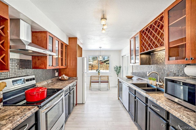 kitchen featuring wall chimney exhaust hood, sink, decorative light fixtures, appliances with stainless steel finishes, and light stone countertops