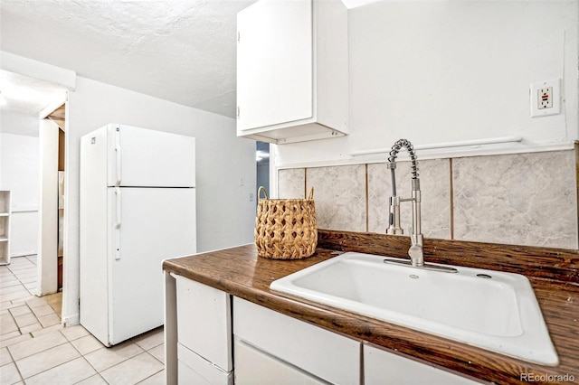 kitchen featuring sink, white cabinetry, a textured ceiling, light tile patterned floors, and white fridge