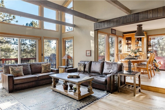 living room with beam ceiling, a high ceiling, and light hardwood / wood-style floors