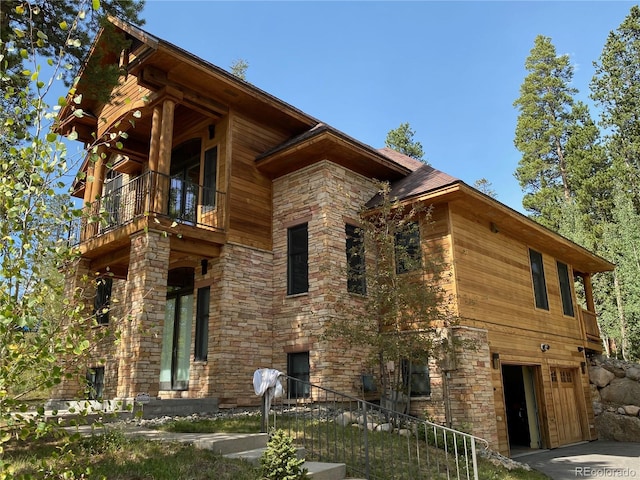 view of side of property with stone siding, a balcony, and an attached garage