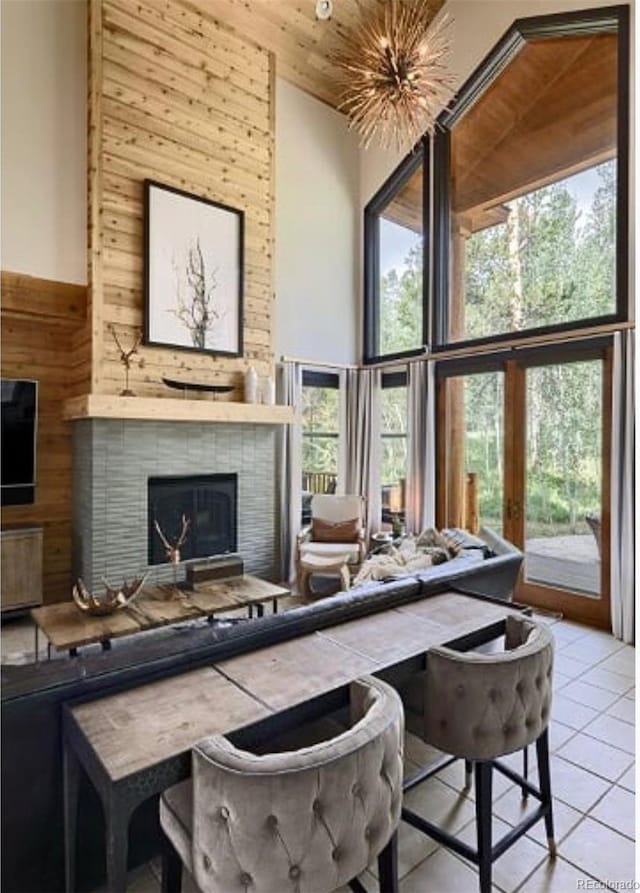 interior space featuring a brick fireplace, wood walls, a towering ceiling, and light tile patterned floors