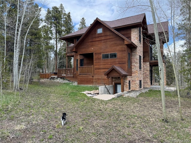 back of property with a balcony, stone siding, a wooden deck, and a yard