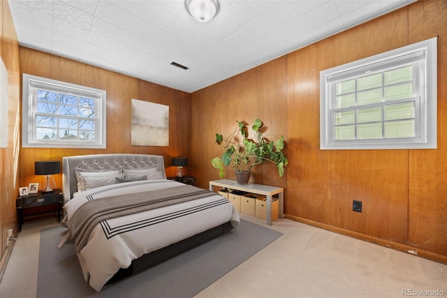 carpeted bedroom with wood walls, multiple windows, and visible vents