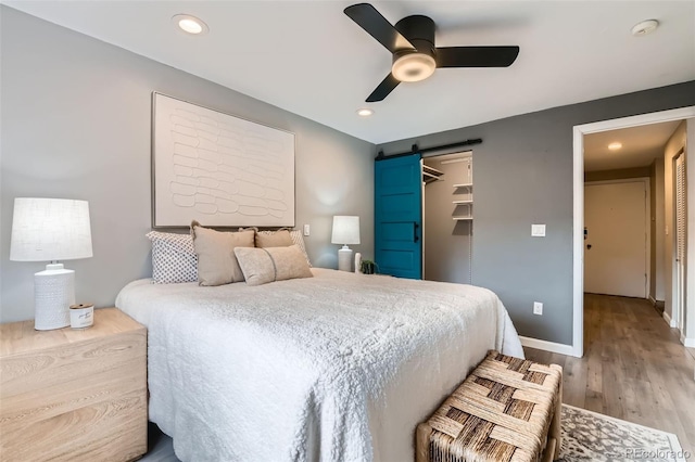 bedroom featuring a barn door, baseboards, ceiling fan, wood finished floors, and recessed lighting