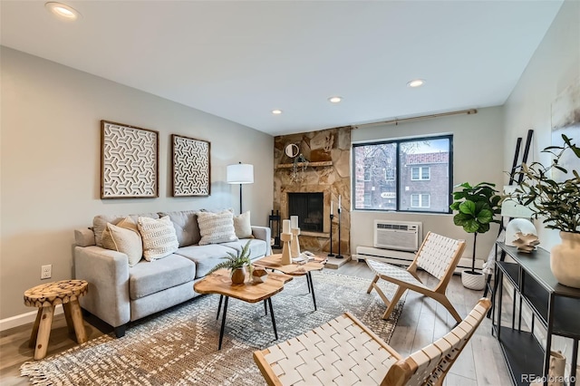 living area with baseboards, wood finished floors, an AC wall unit, a stone fireplace, and recessed lighting